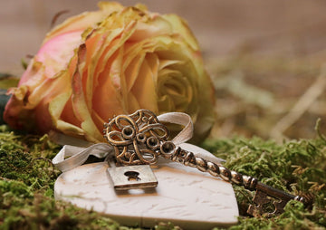 A delicate vintage key and a soft, blooming rose rest on a bed of vibrant green moss. The scene evokes a sense of mystery and romance, blending nature with timeless elegance.