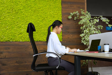 A person sits at a modern office desk, working on a laptop, with a lush green moss wall in the background. The vibrant moss adds a natural, calming touch to the workspace, creating a refreshing contrast to the office setting.